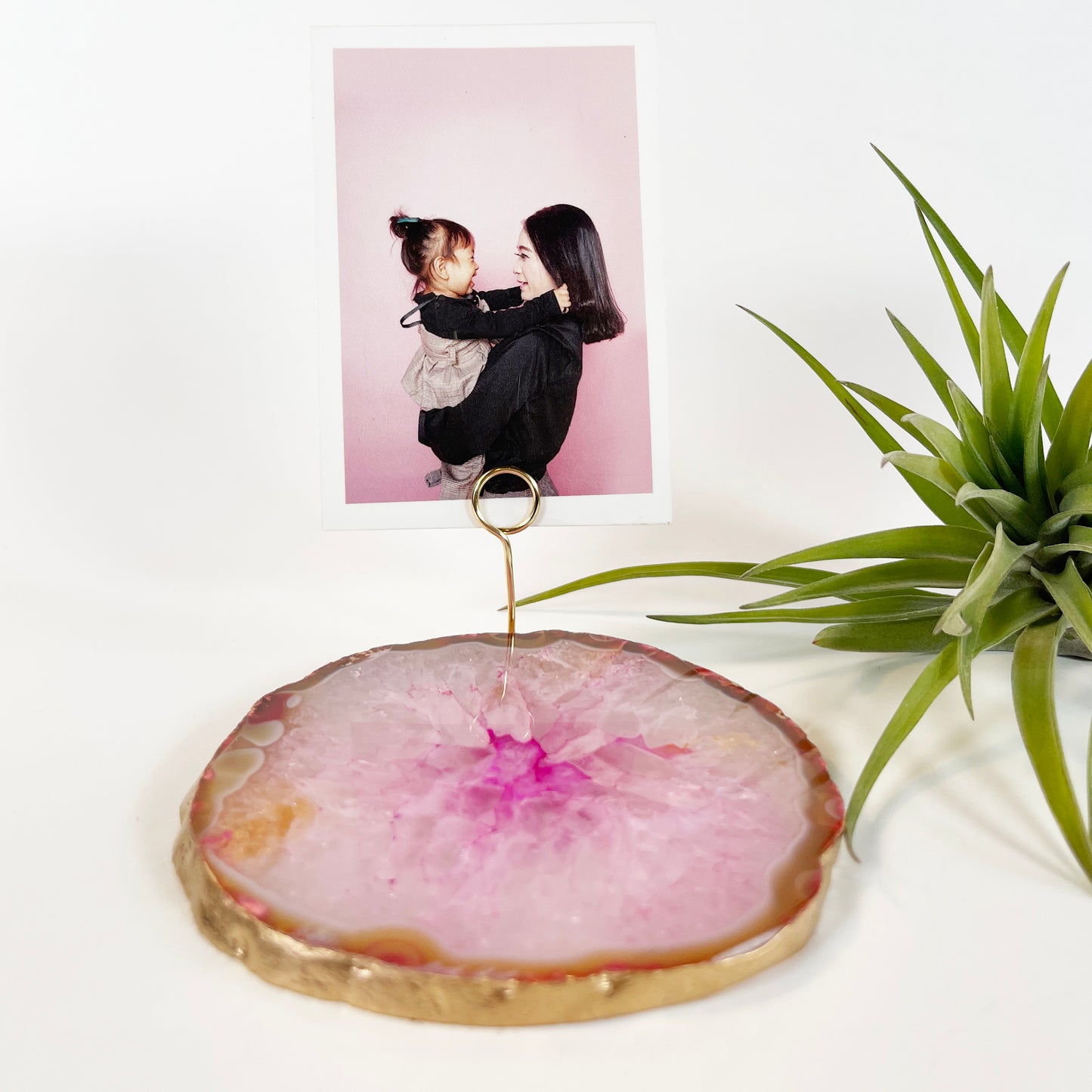 Round Pink Agate with gold rim holding up a picture of a mom and daughter by a gold spiral photo holder